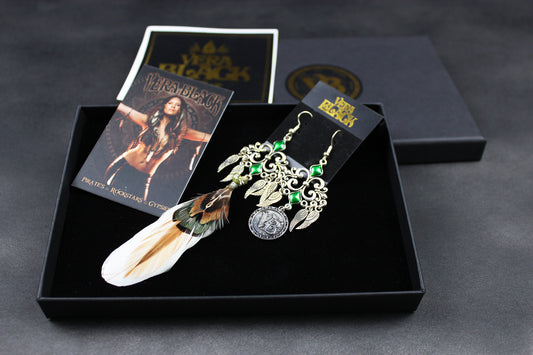 Pair of earrings with feathers and green stones in a black box with packaging on a dark background