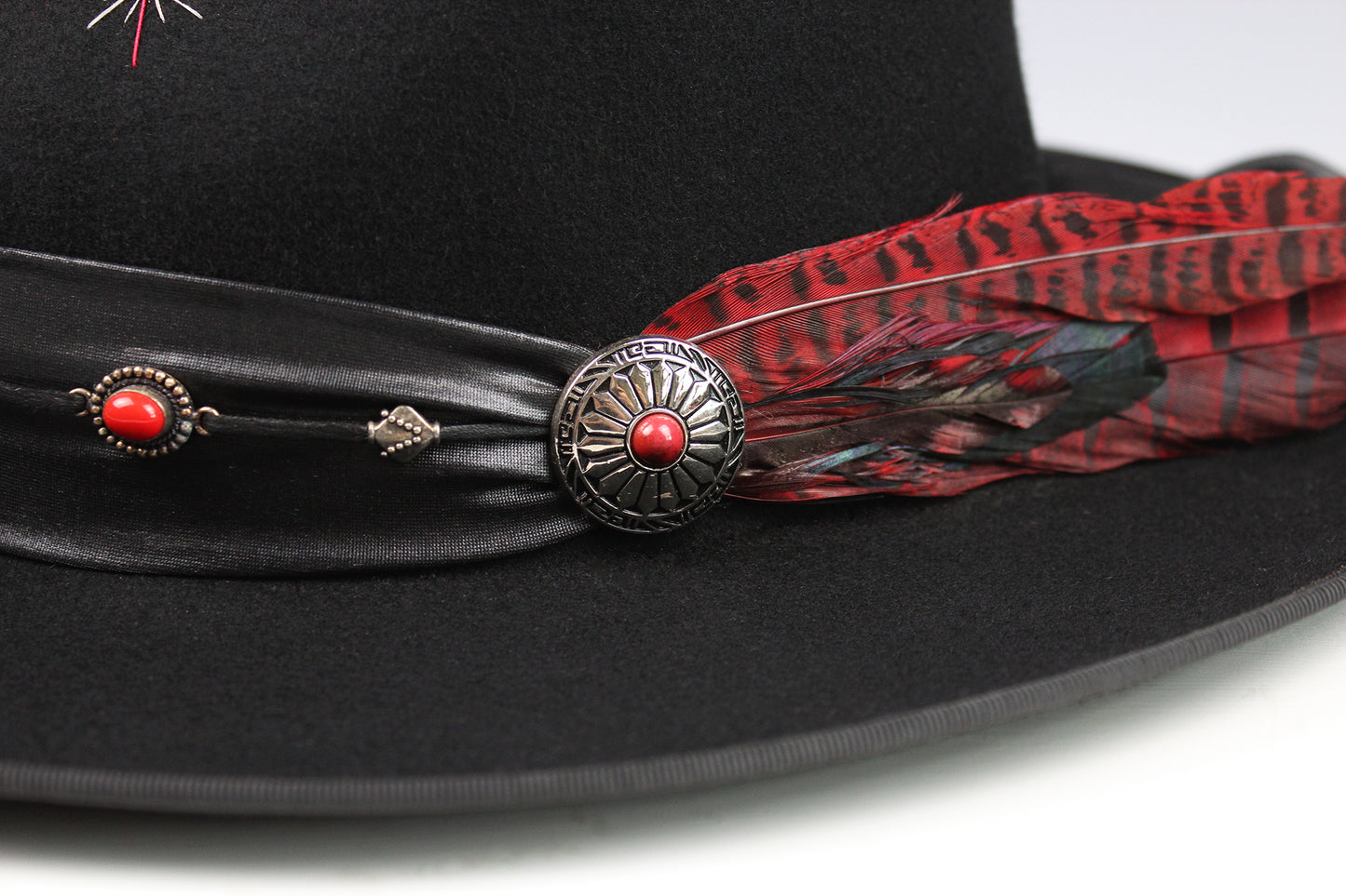 Black hat with red feather and decorative band on a white background