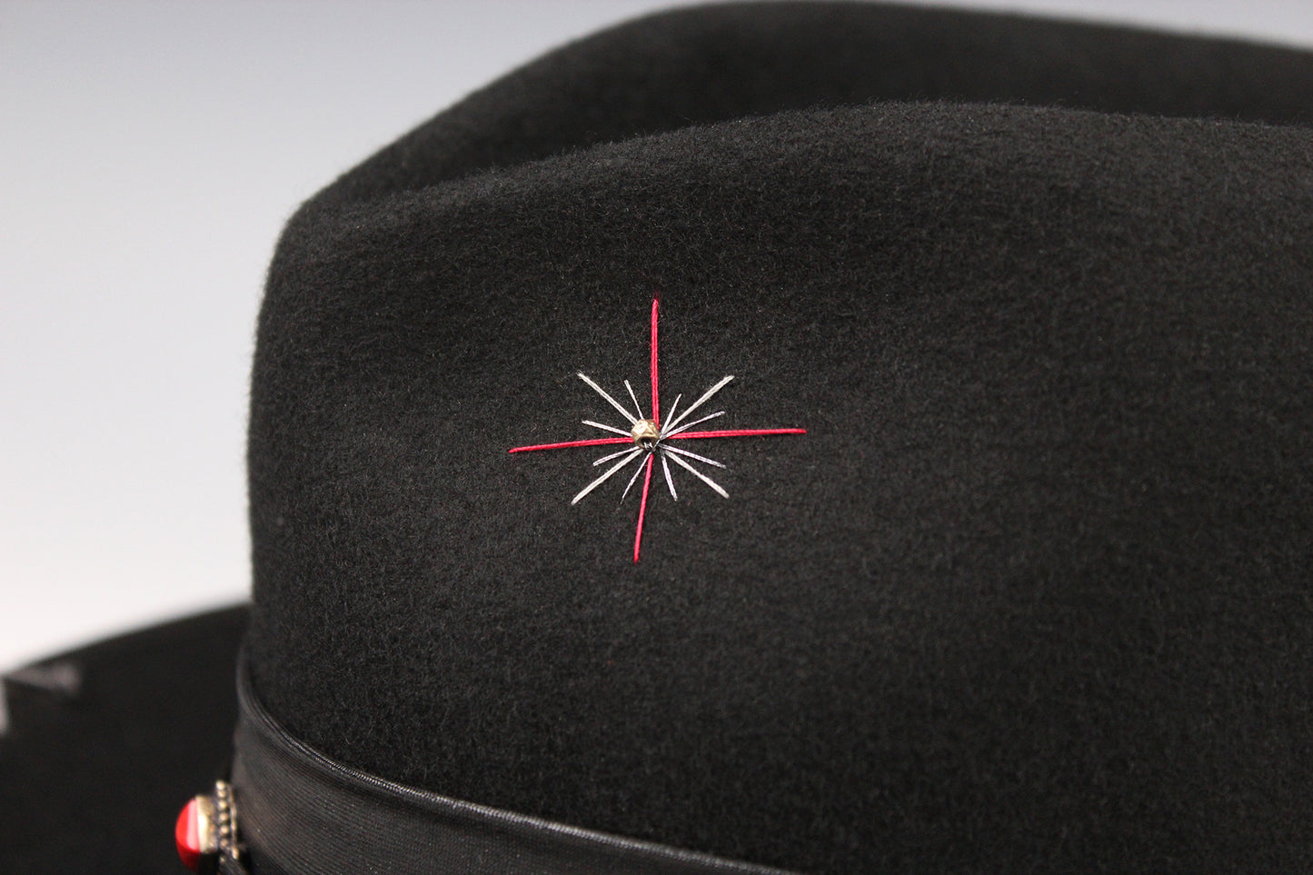 Black hat with a red and white embroidered star design on a gray background