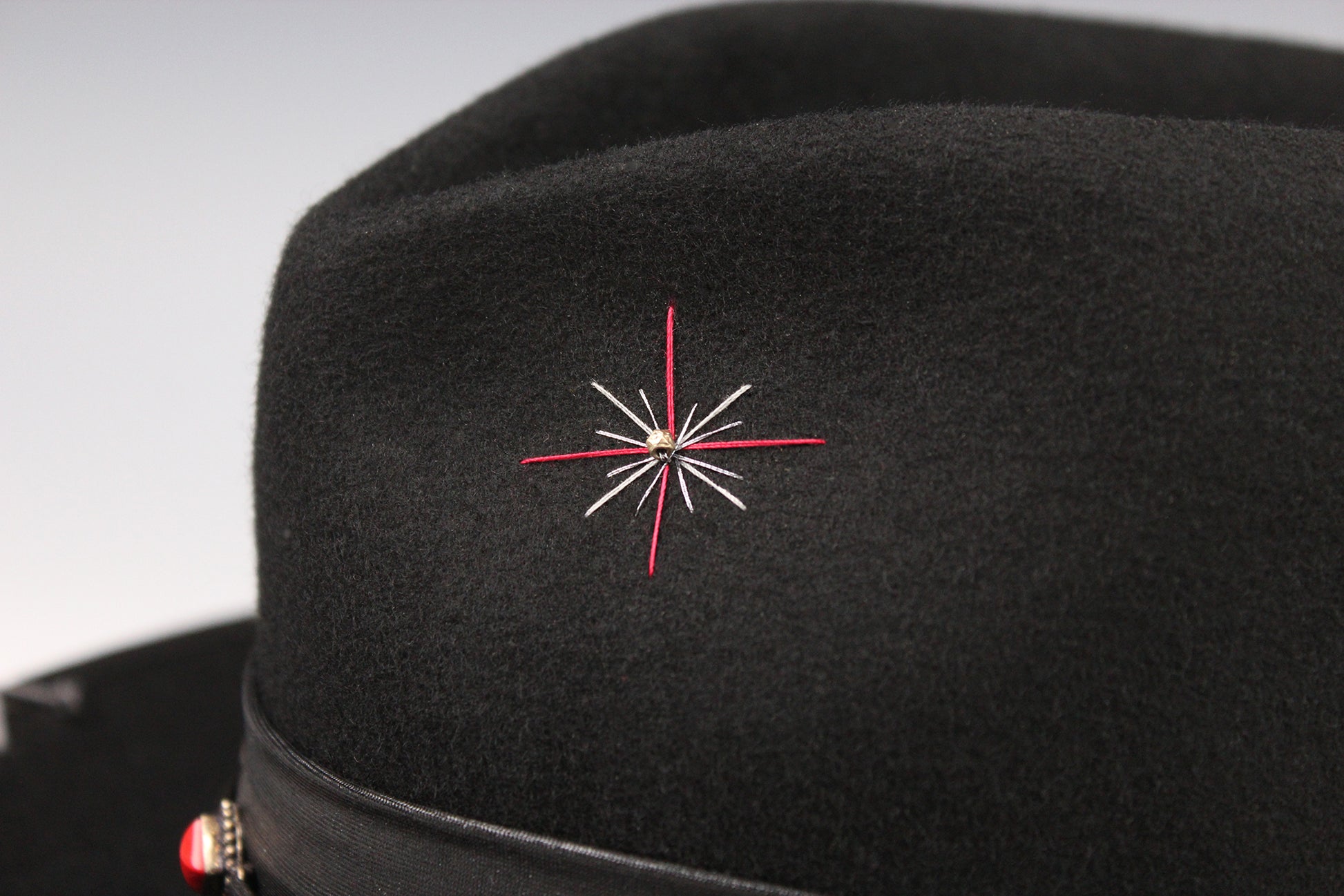 Black hat with a red and white embroidered star design on a gray background