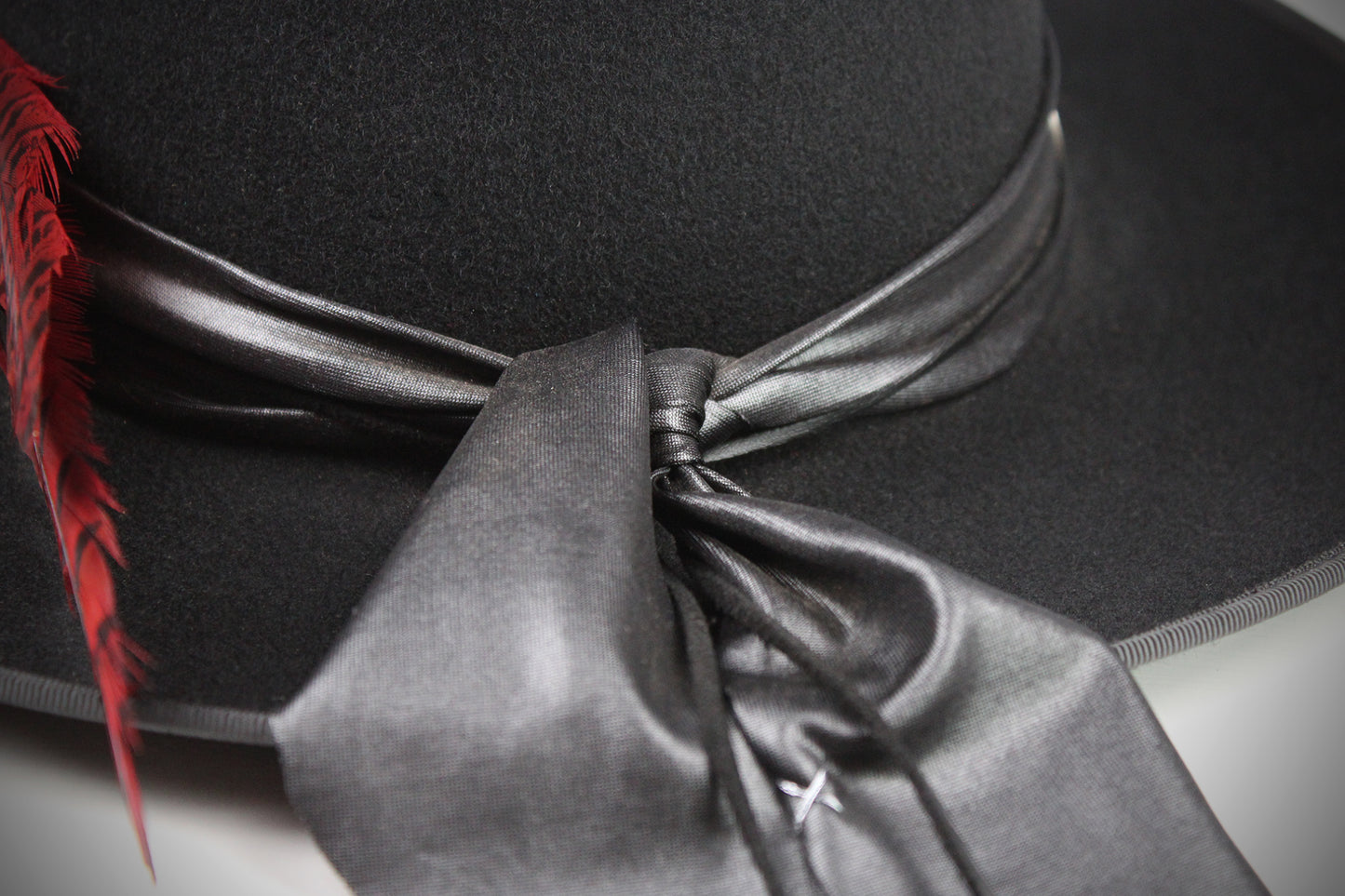 Black hat with a red feather and gray ribbon on a neutral background