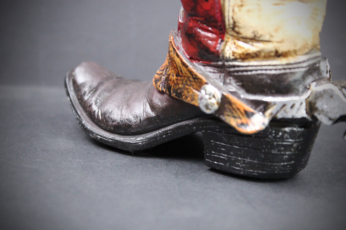 A close-up of a western-style boot with a dark brown leather foot, black heel, and a distressed red, beige, and brown shaft, photographed against a dark gray background.