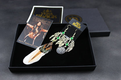 Pair of earrings with feathers and green stones in a black box with packaging on a dark background
