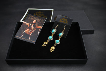 Gold and turquoise earrings in a black box with branded cards on a dark background