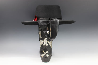 Black cowboy hat with decorative band featuring skulls and crossbones on a gray background