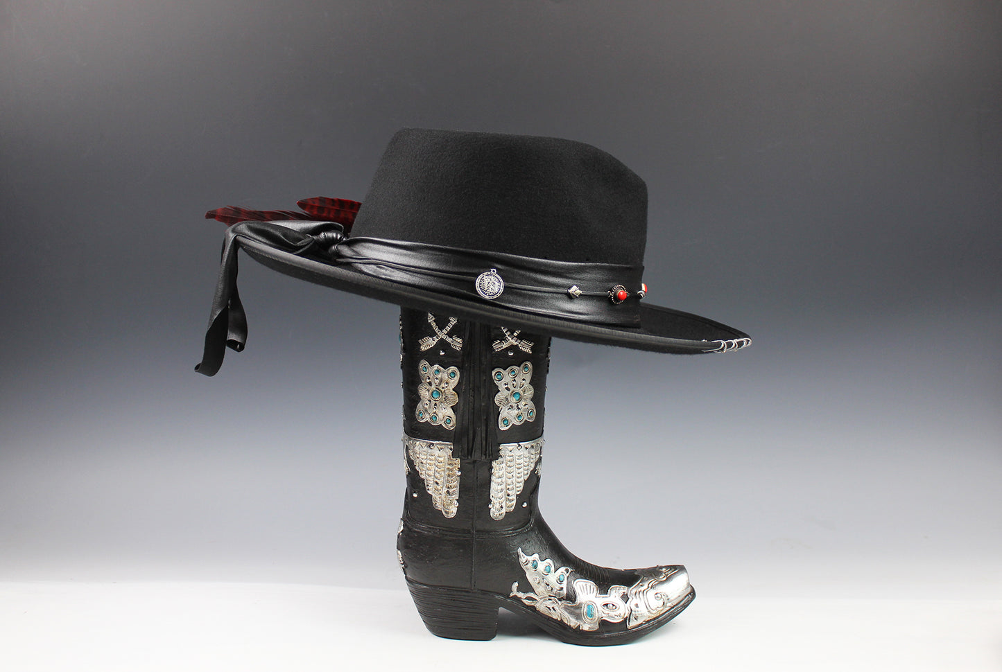 Black cowboy hat with decorative band and black boot with embellishments on a gray background