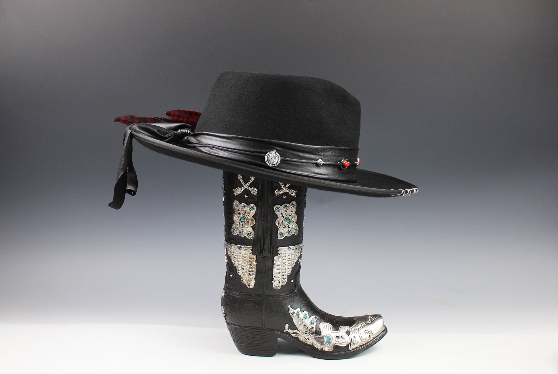 Black cowboy hat with decorative band and black boot with embellishments on a gray background