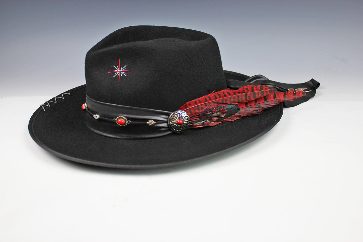 Black cowboy hat with decorative band and feather on a gray background