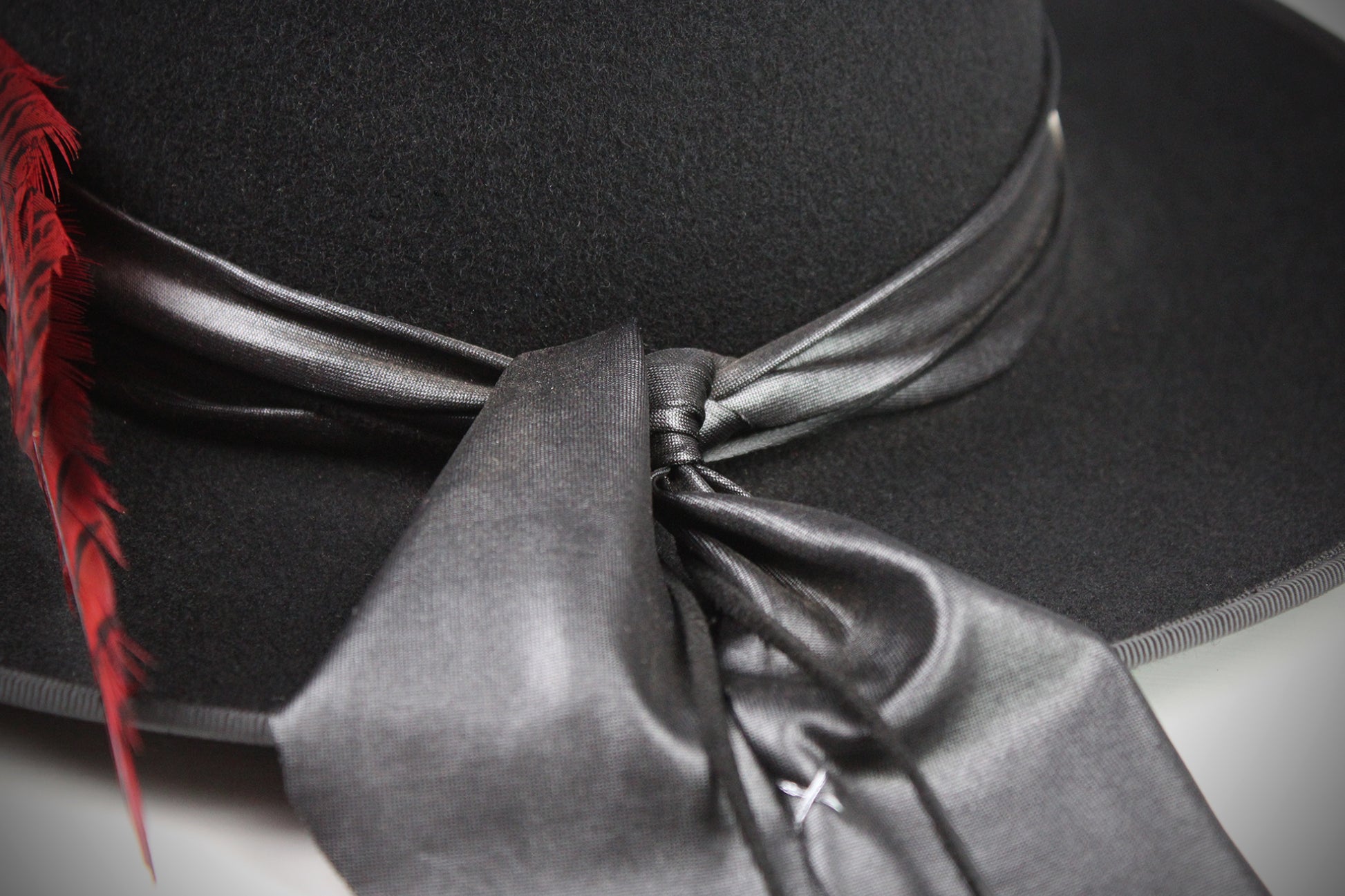 Black hat with a red feather and gray ribbon on a neutral background