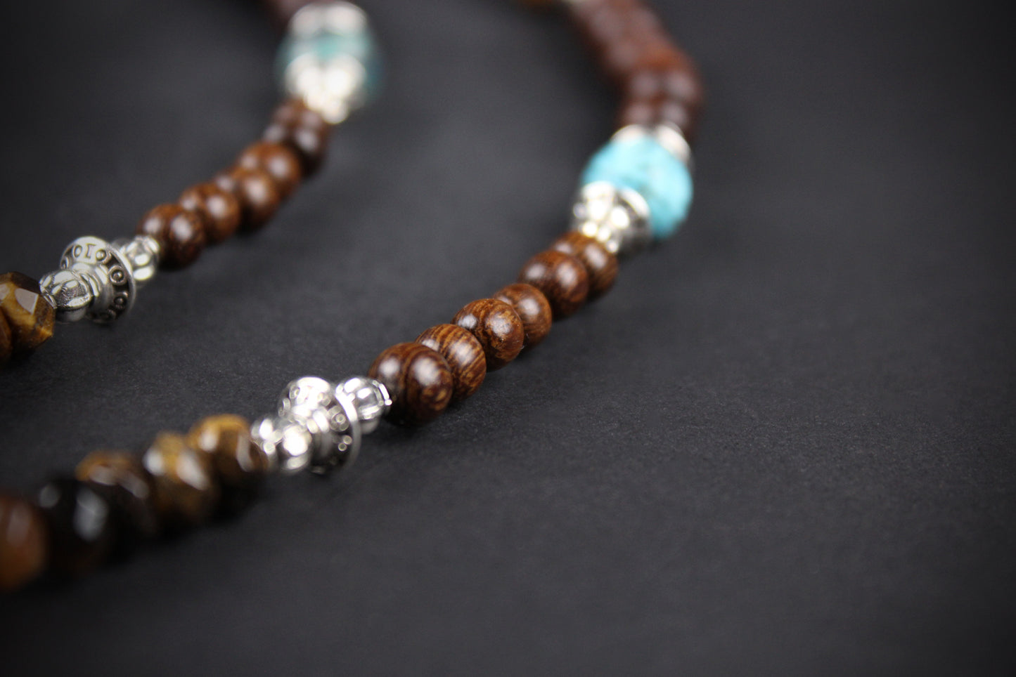 Necklace with brown, turquoise, and silver beads on a dark background