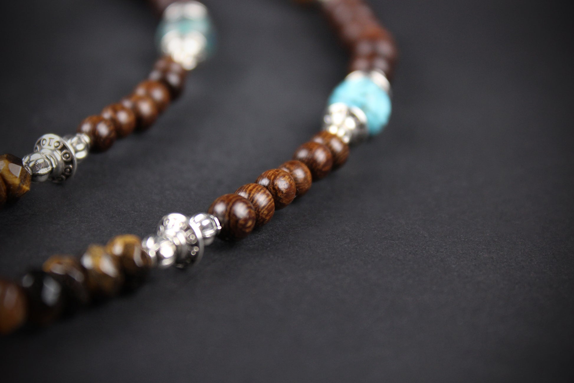 Necklace with brown, turquoise, and silver beads on a dark background
