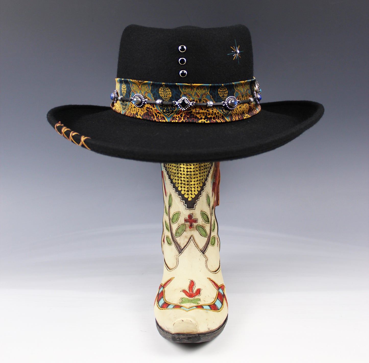 Decorative black hat with colorful band and embroidered white boot on a gray background