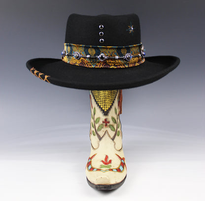 Decorative black hat with colorful band and embroidered white boot on a gray background