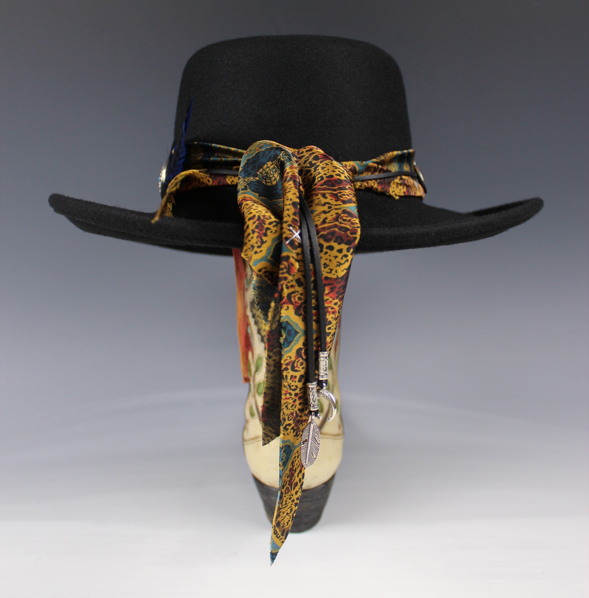 Black cowboy hat with a colorful bandana tied around it on a gray background
