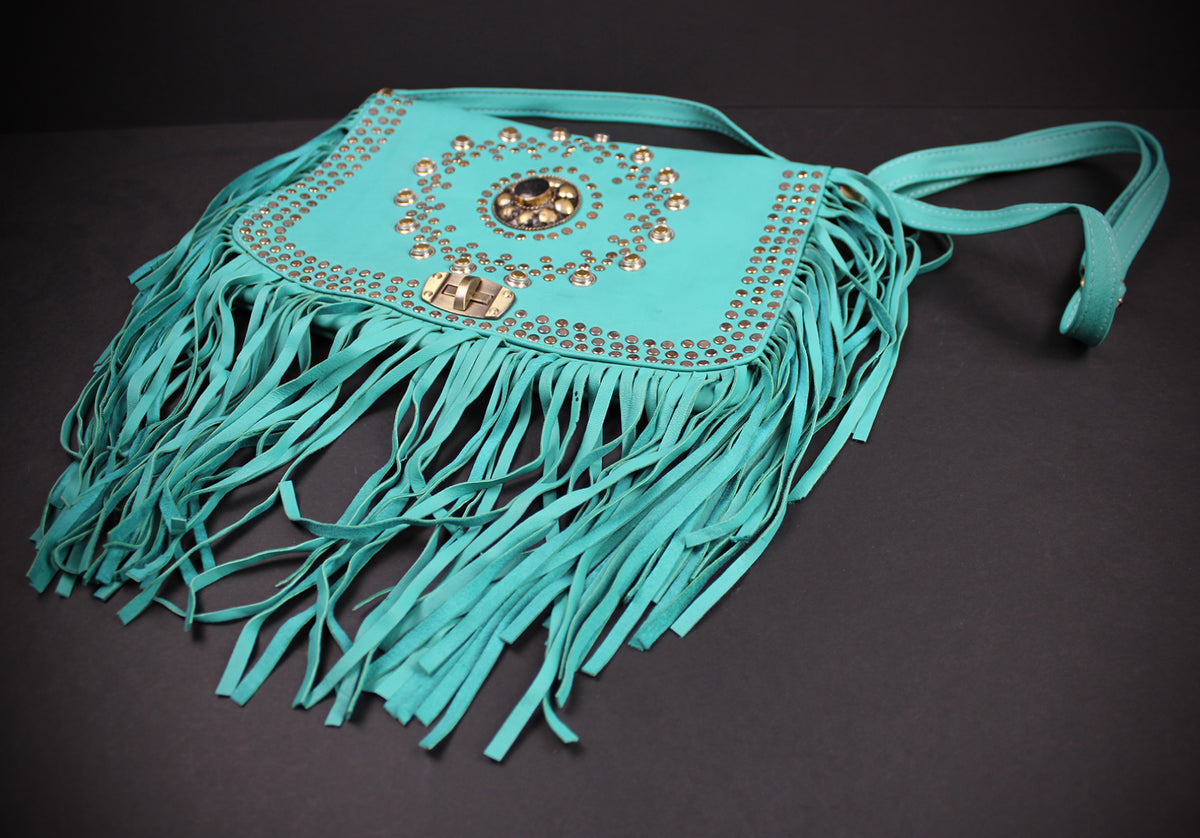 A turquoise fringe shoulder bag with gold-tone studs and a central medallion embellishment, displayed on a dark background.