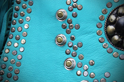 Close-up of a turquoise faux-leather surface decorated with multiple rows of silver-toned studs and two larger central concho-style embellishments.