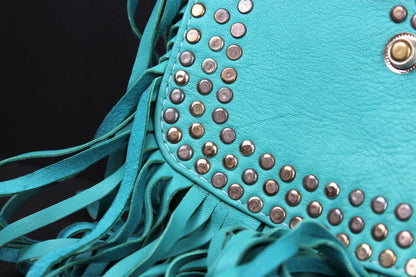 Close-up of a turquoise faux-leather fringe bag decorated with rows of metallic silver studs and a silver snap button, set against a solid black background.