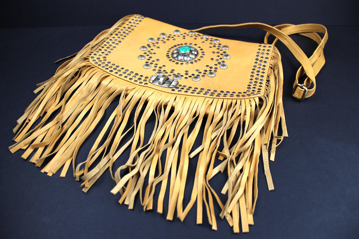 A tan leather fringe purse with a central turquoise and silver concho embellishment, photographed on a dark navy background.