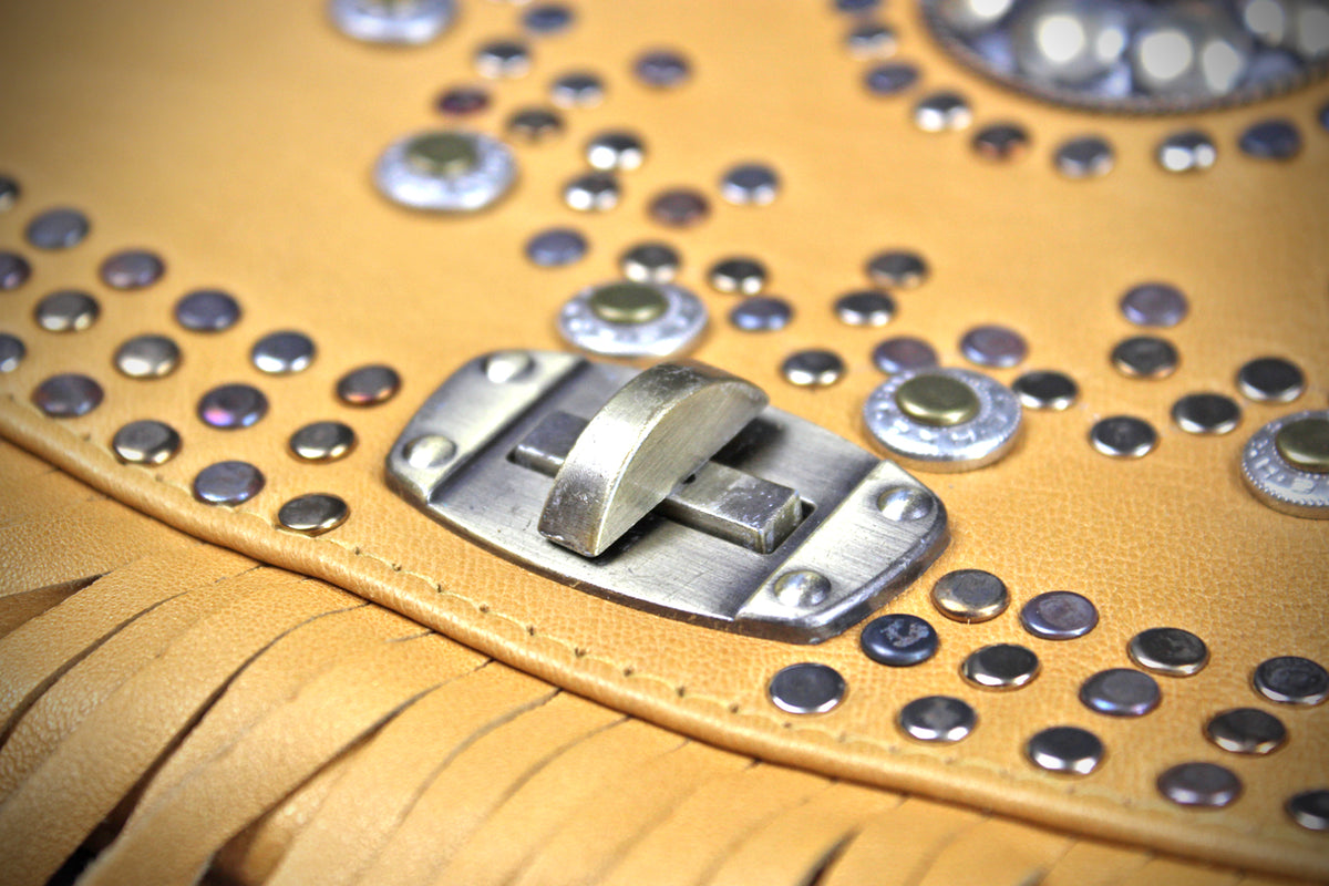 Close-up of a tan leather fringe accessory with silver studs and a metal clasp, photographed in high detail.