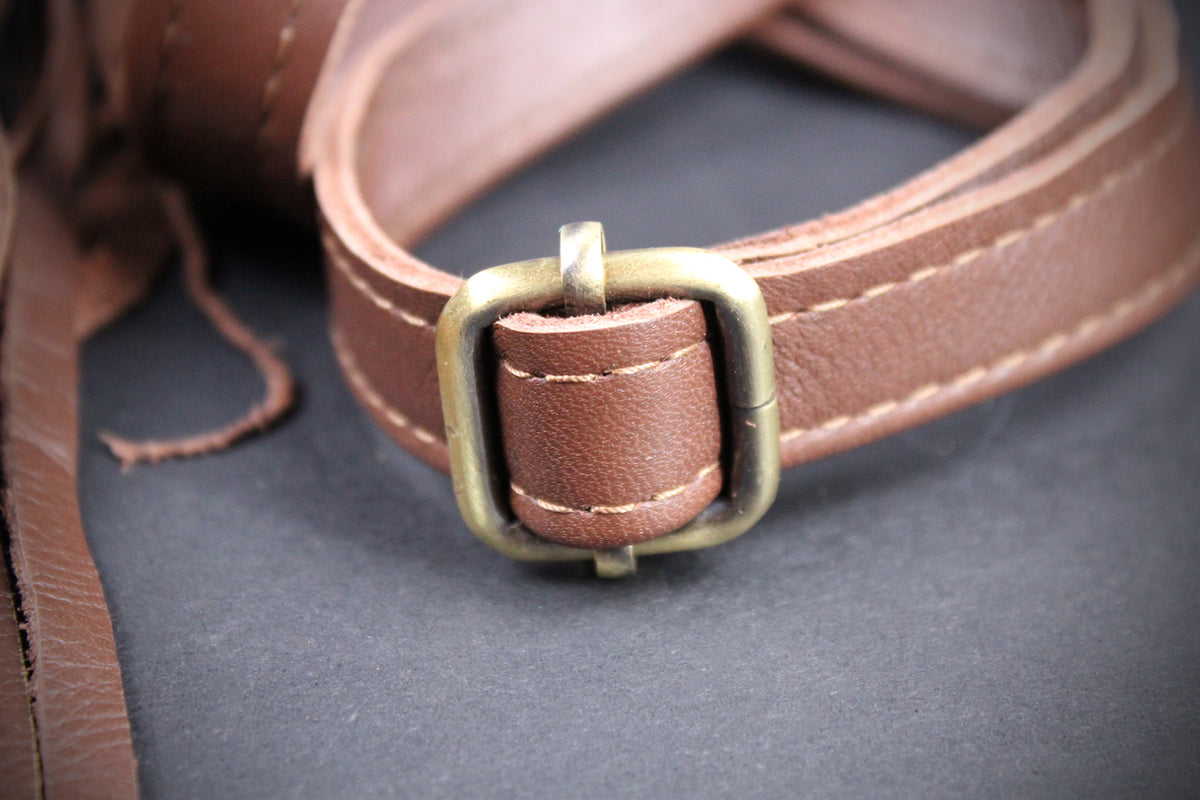 A close-up of a brown leather strap with a brass buckle, resting on a dark gray textured surface.