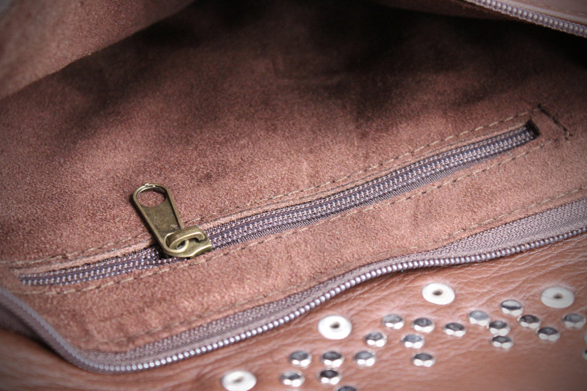 Close-up of a brown suede or faux-suede interior pocket with a silver zipper and a small gold-toned zipper pull, alongside a matching brown exterior surface with rhinestone embellishments.