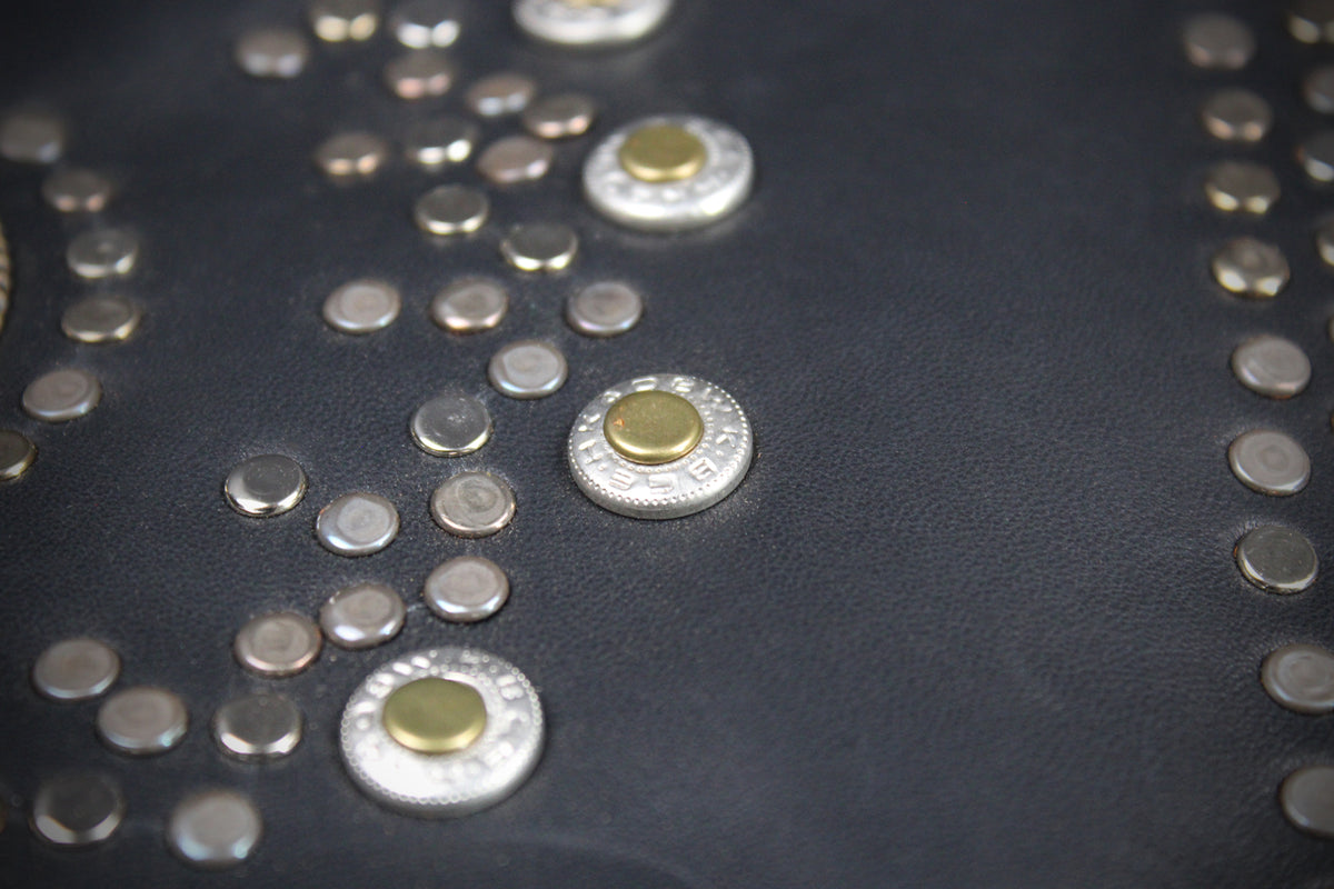 Close-up of a black leather surface decorated with multiple silver-tone studs and a few larger studs featuring a gold-tone center.