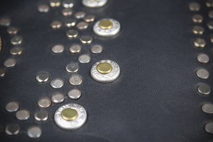 Close-up of a black leather surface decorated with multiple silver-tone studs and a few larger studs featuring a gold-tone center.