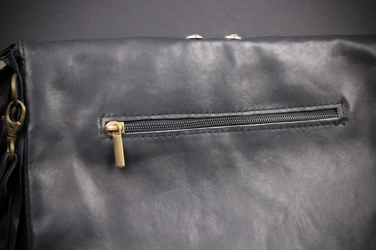 Close-up of a black leather or faux-leather bag with a horizontal zippered pocket and gold-tone zipper pull, shown against a dark background.