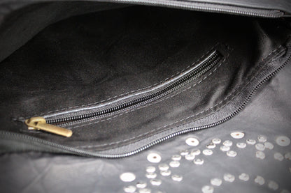 Close-up of a black leather or faux-leather bag interior showing a zippered pocket with a gold-tone zipper pull and scattered silver studs on the exterior surface.