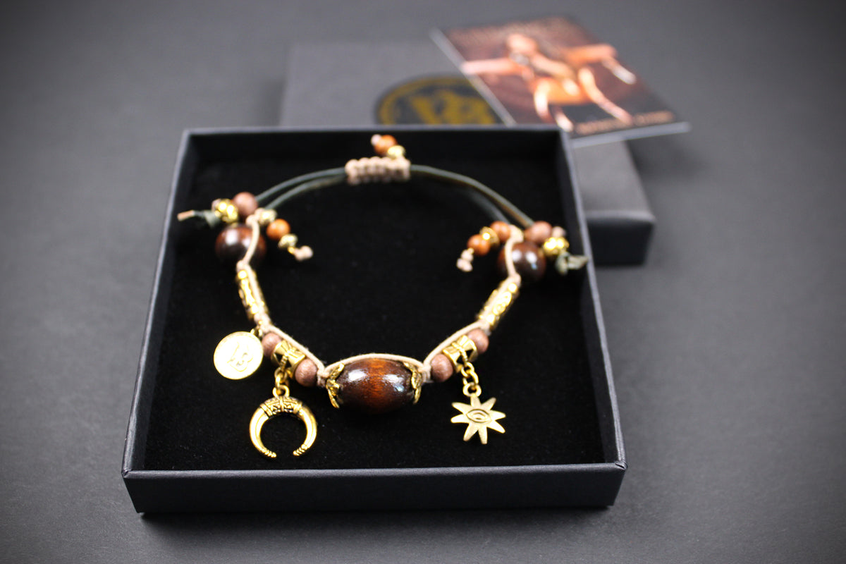 A beaded bracelet with gold-toned charms, including a crescent moon and star, displayed in an open black presentation box on a dark background.