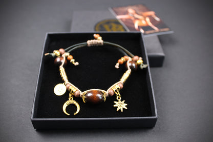 A beaded bracelet with gold-toned charms, including a crescent moon and star, displayed in an open black presentation box on a dark background.