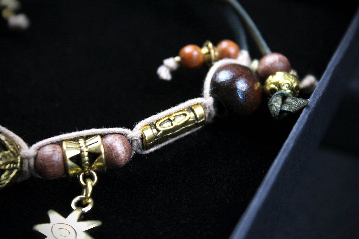 A close-up of a beaded necklace or bracelet featuring dark brown wooden beads, metallic gold-toned cylindrical spacers, and a dangling star charm, displayed on a black velvet surface.
