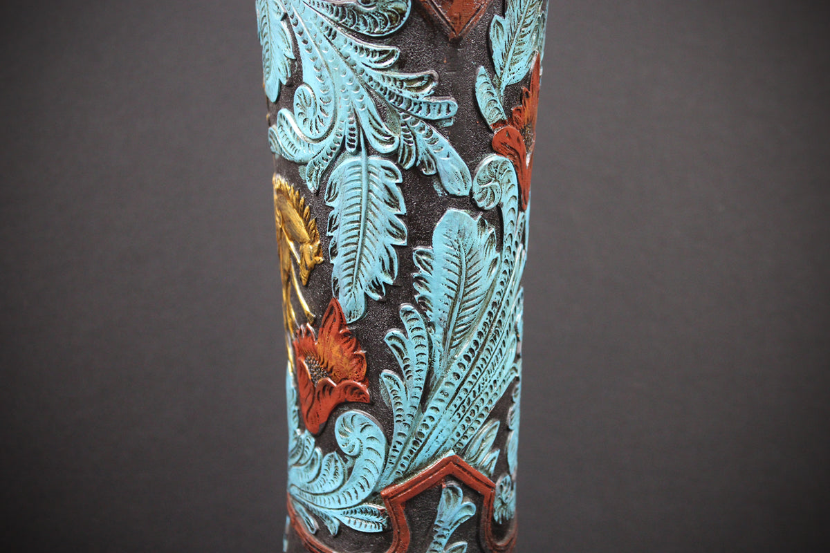 A close-up of a hand-tooled western-style column featuring intricate floral and leaf designs in turquoise, rust red, and gold over a dark brown carved wood background, set against a dark gray backdrop.