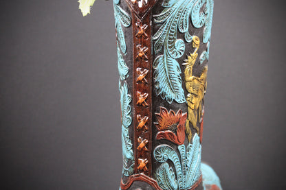 Close-up of a western boot shaft featuring turquoise blue foil, brown tooled leather, and gold and red floral embroidery against a dark background.