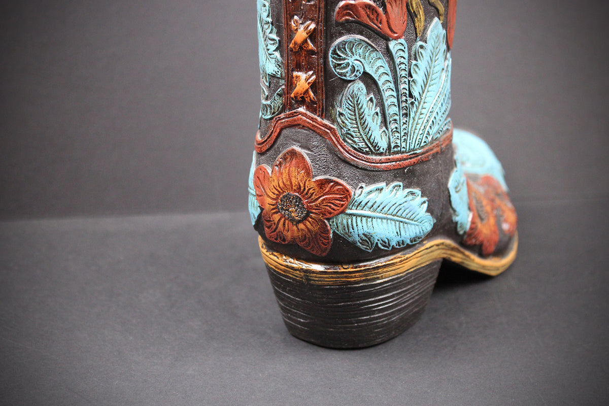 A close-up of the heel and side of a decorated cowboy boot on a dark gray background. The boot features turquoise blue floral and leaf tooling, reddish-brown floral accents, and a dark brown textured shaft with a gold-toned stacked heel.