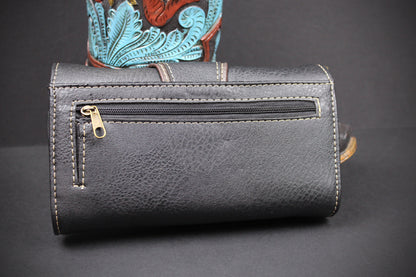 A black textured leather pouch with a horizontal zippered pocket and contrast stitching, shown against a dark background with a colorful patterned object partially visible behind it.
