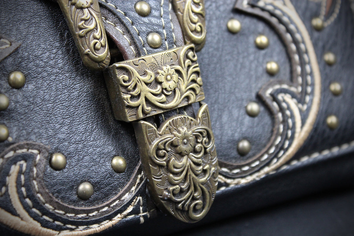 Close-up of a dark brown leather handbag with ornate embossed stitching, brass studs, and a decorative antique bronze buckle with floral scrollwork.