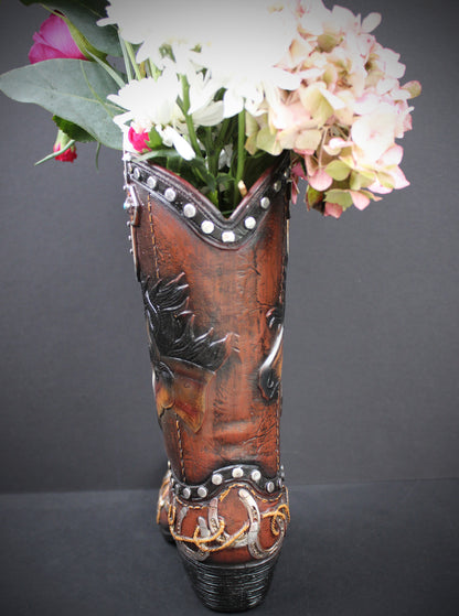 A brown leather cowboy boot vase filled with white and pink flowers, set against a dark gray background.