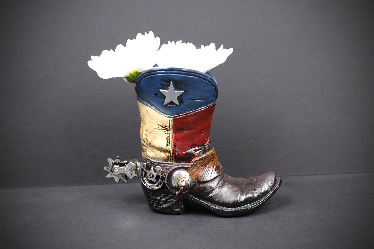 A cowboy boot planter styled with the Texas flag colors and a silver star, holding two white flowers, set against a dark gray background.