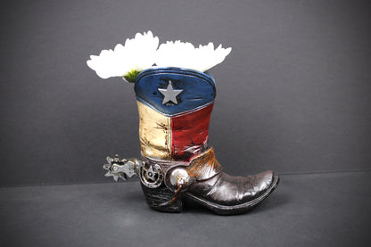 A cowboy boot planter styled with the Texas flag colors and a silver star, holding two white flowers, set against a dark gray background.
