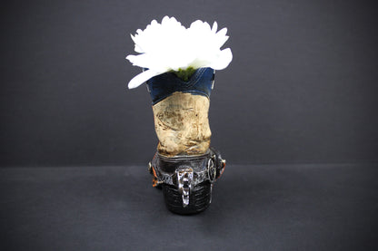 A gothic-style high-heeled shoe vase decorated with a blue denim upper, a weathered wood midsection, and a black faux-leather heel, holding a white flower against a dark gray background.