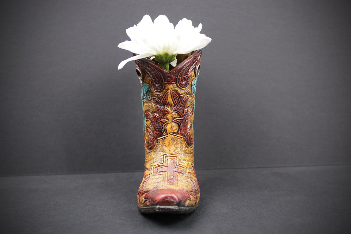 A decorative cowboy boot-shaped vase filled with a single white flower, set against a dark gray background.