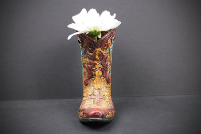 A decorative cowboy boot-shaped vase filled with a single white flower, set against a dark gray background.