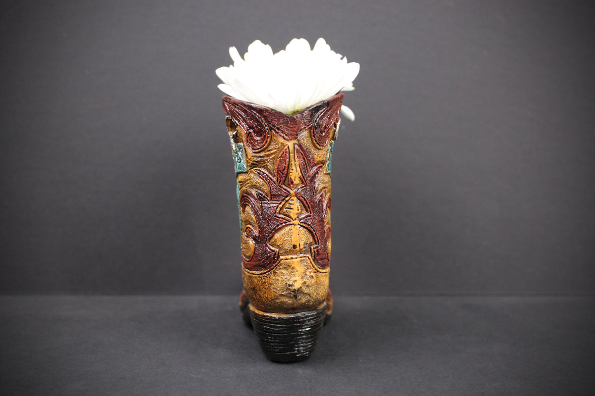 A decorative ceramic vase shaped like a western boot, featuring a brown and gold embossed western pattern, with a white flower inserted at the top, set against a dark gray background.