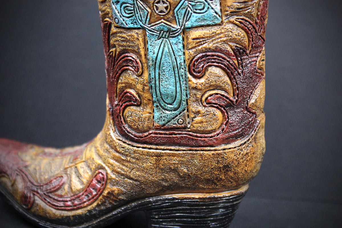 A close-up of a western cowboy boot showing the shaft and heel, decorated with embossed brown scrollwork and turquoise blue accents on a distressed tan background.
