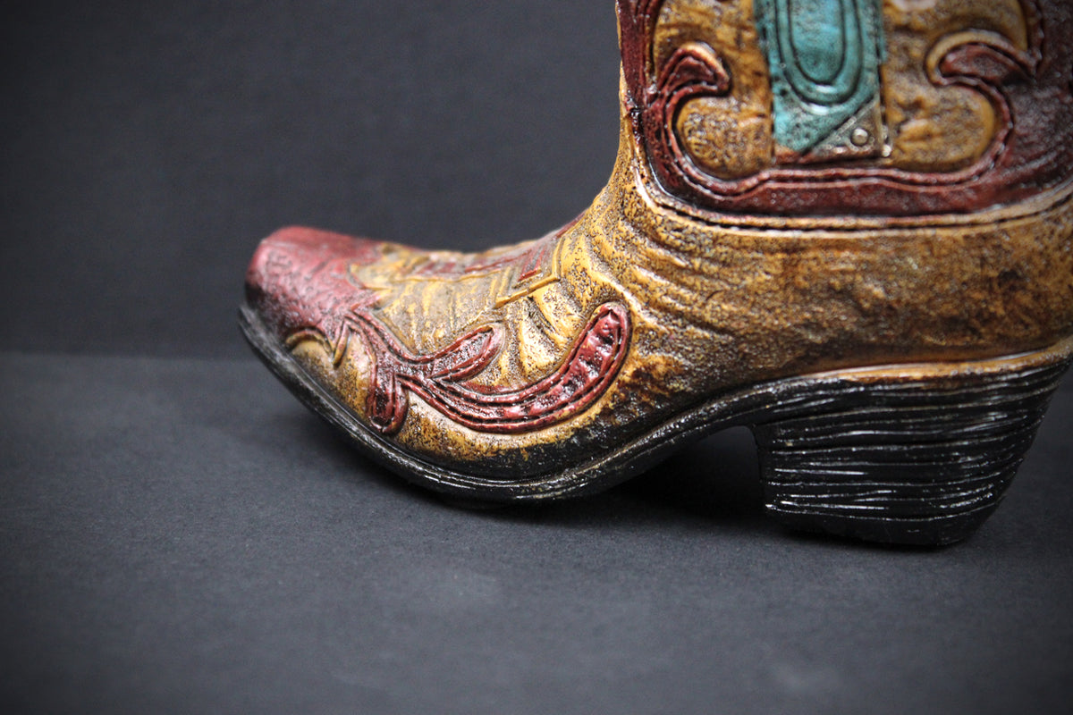 A close-up of a western-style cowboy boot with a distressed gold and brown leather finish, featuring red embroidered detailing on the toe and shaft, and a turquoise accent near the top.