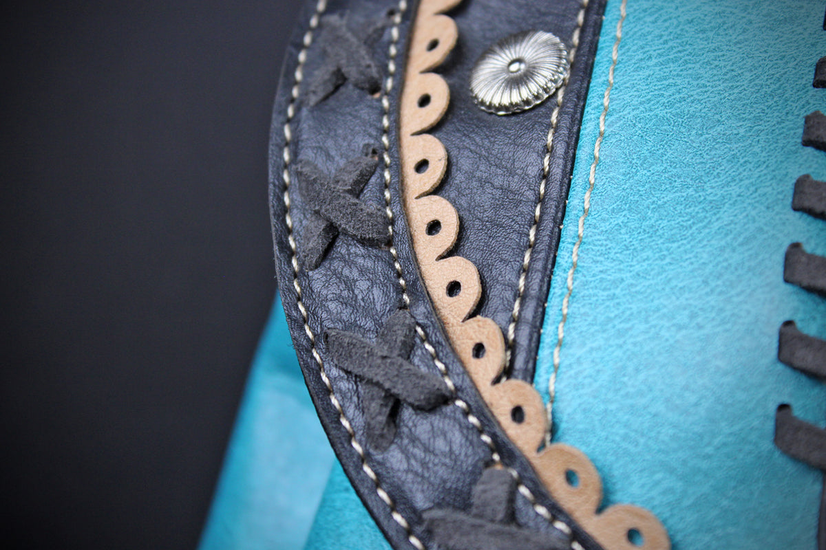 Close-up detail of a turquoise leather item featuring dark charcoal gray leather trim with whipstitching, a scalloped cutout edge, and a silver-toned decorative rivet.