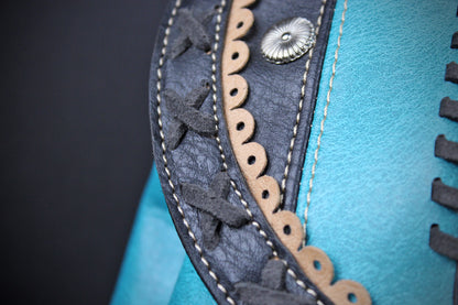 Close-up detail of a turquoise leather item featuring dark charcoal gray leather trim with whipstitching, a scalloped cutout edge, and a silver-toned decorative rivet.