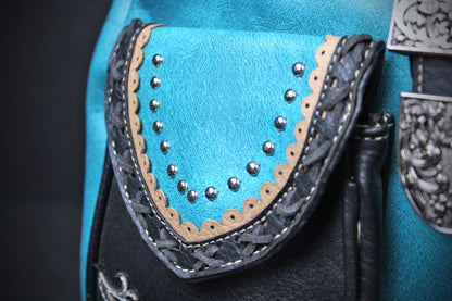 Close-up detail of a turquoise blue leather pouch with braided trim, silver studs, and a dark leather edge on a black background.