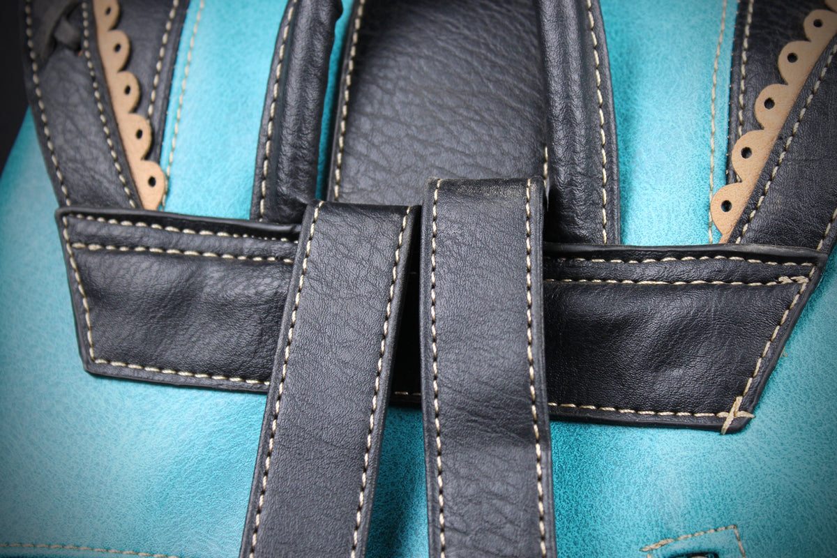 Close-up detail of a backpack showing black textured leather straps with white contrast stitching over a turquoise blue fabric body.